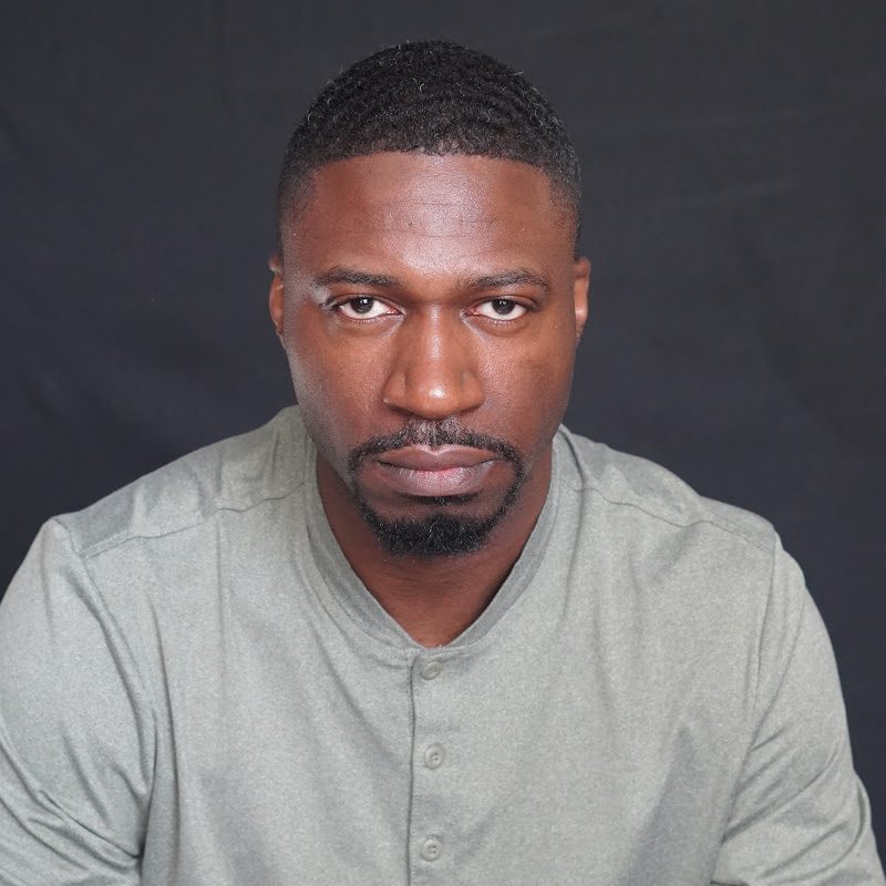 NovA, Philadelphia rapper, in a grey shirt looking straight into the camera against a dark backdrop